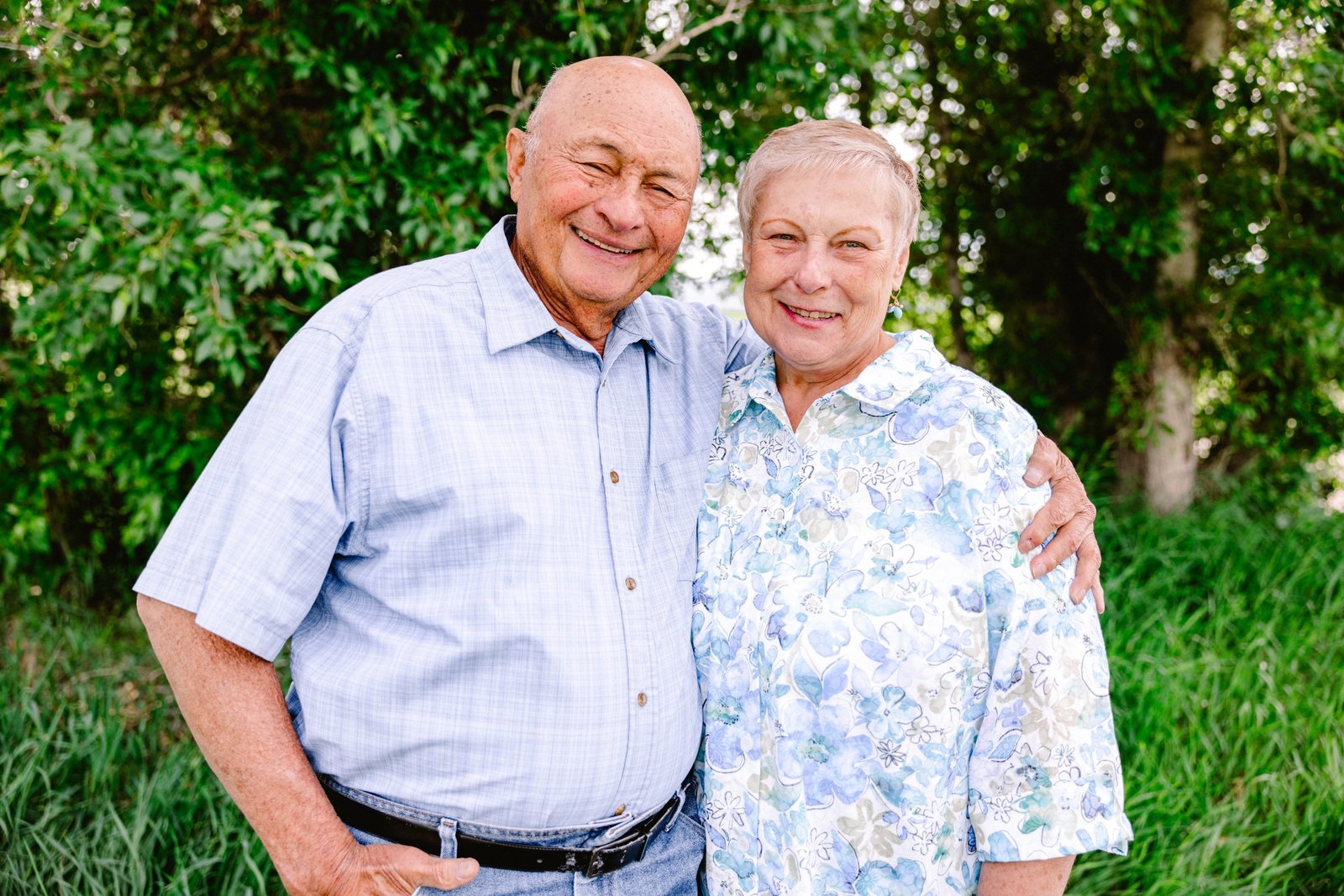 Foalima Hokum and his wife smiling together outdoors in front of green trees.